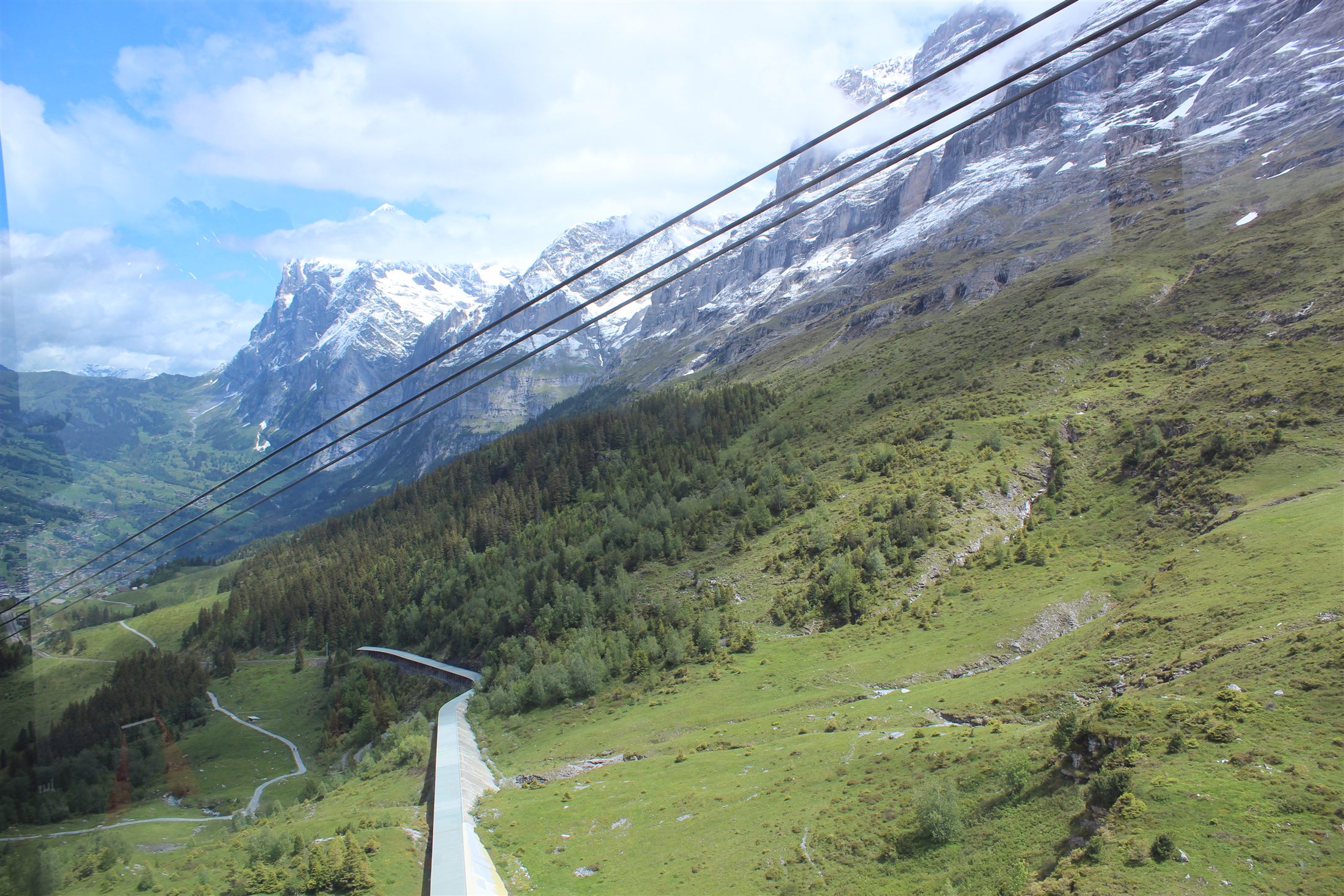Múltiplas cabines do teleférico Eiger Express na linha, com a ferrovia de cremalheira e Grindelwald no fundo do vale