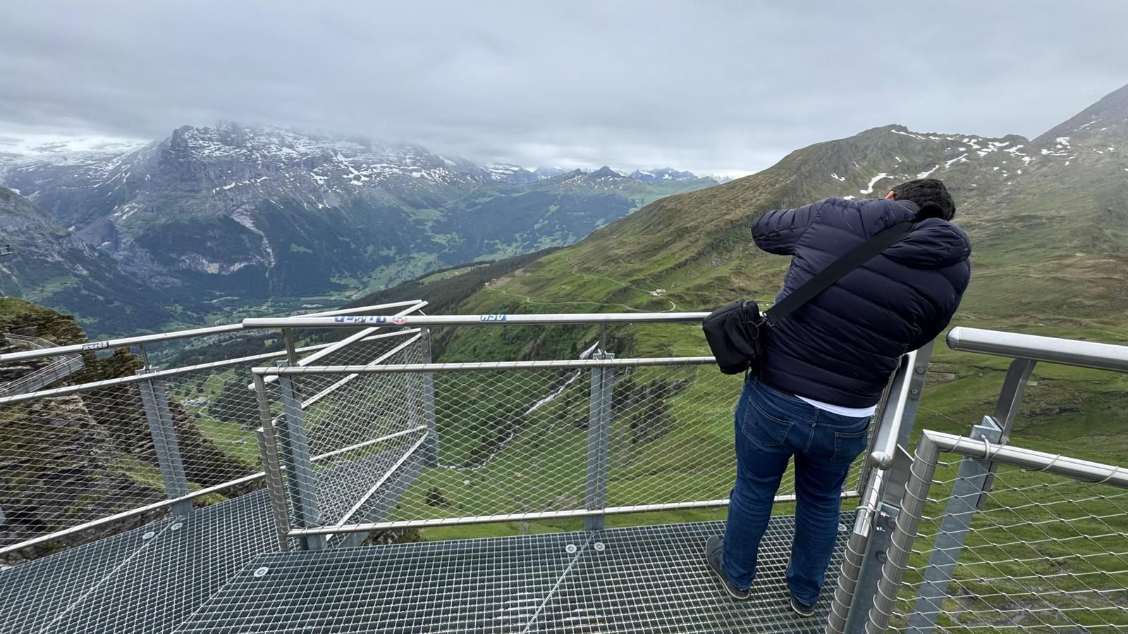 Visitante de costas na passarela de grade metálica da First Cliff Walk, suspensa sobre o vale de Grindelwald com montanhas ao fundo