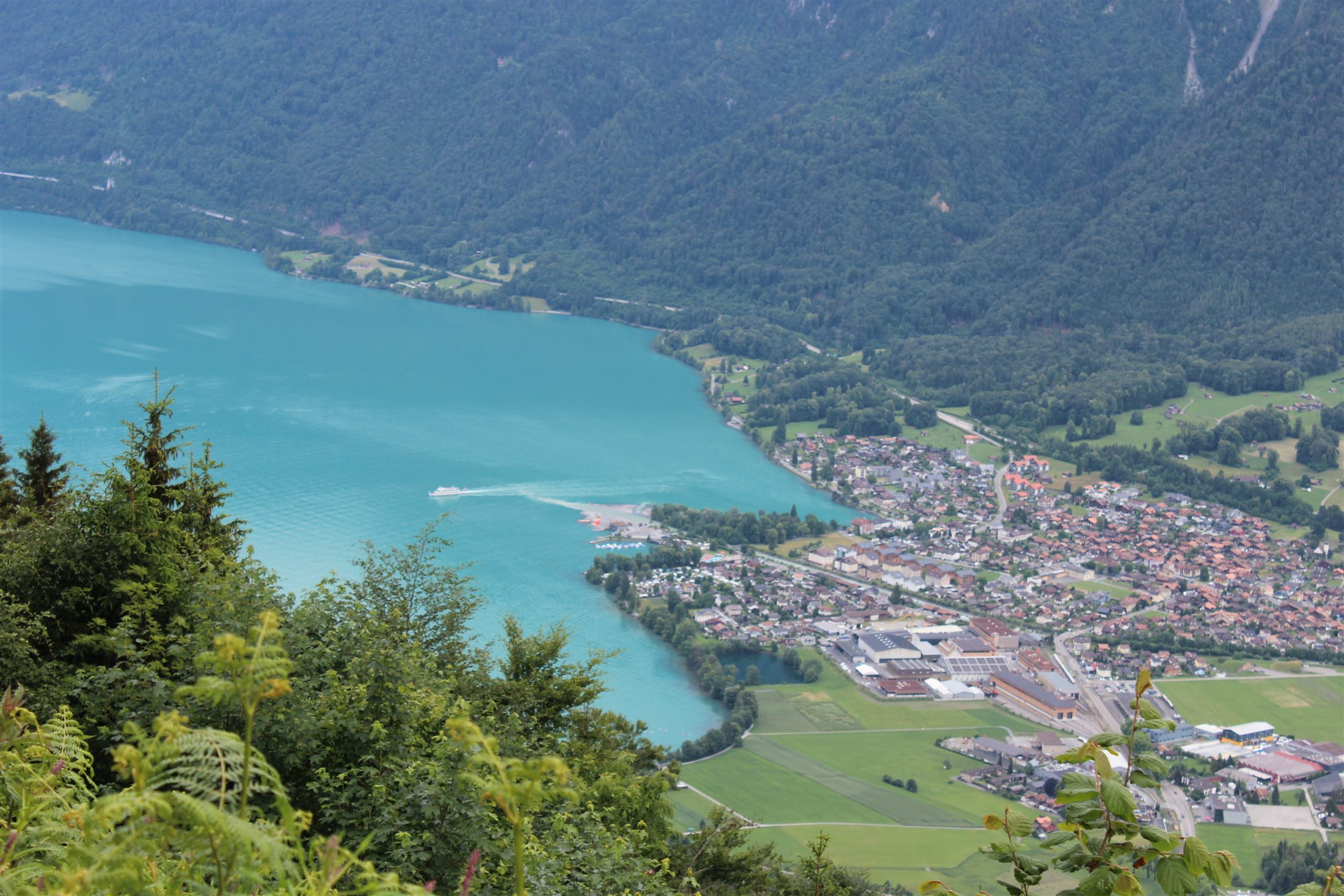 Vista aérea do Lago de Brienz turquesa com a cidade de Brienz à direita e um barco cruzando o lago