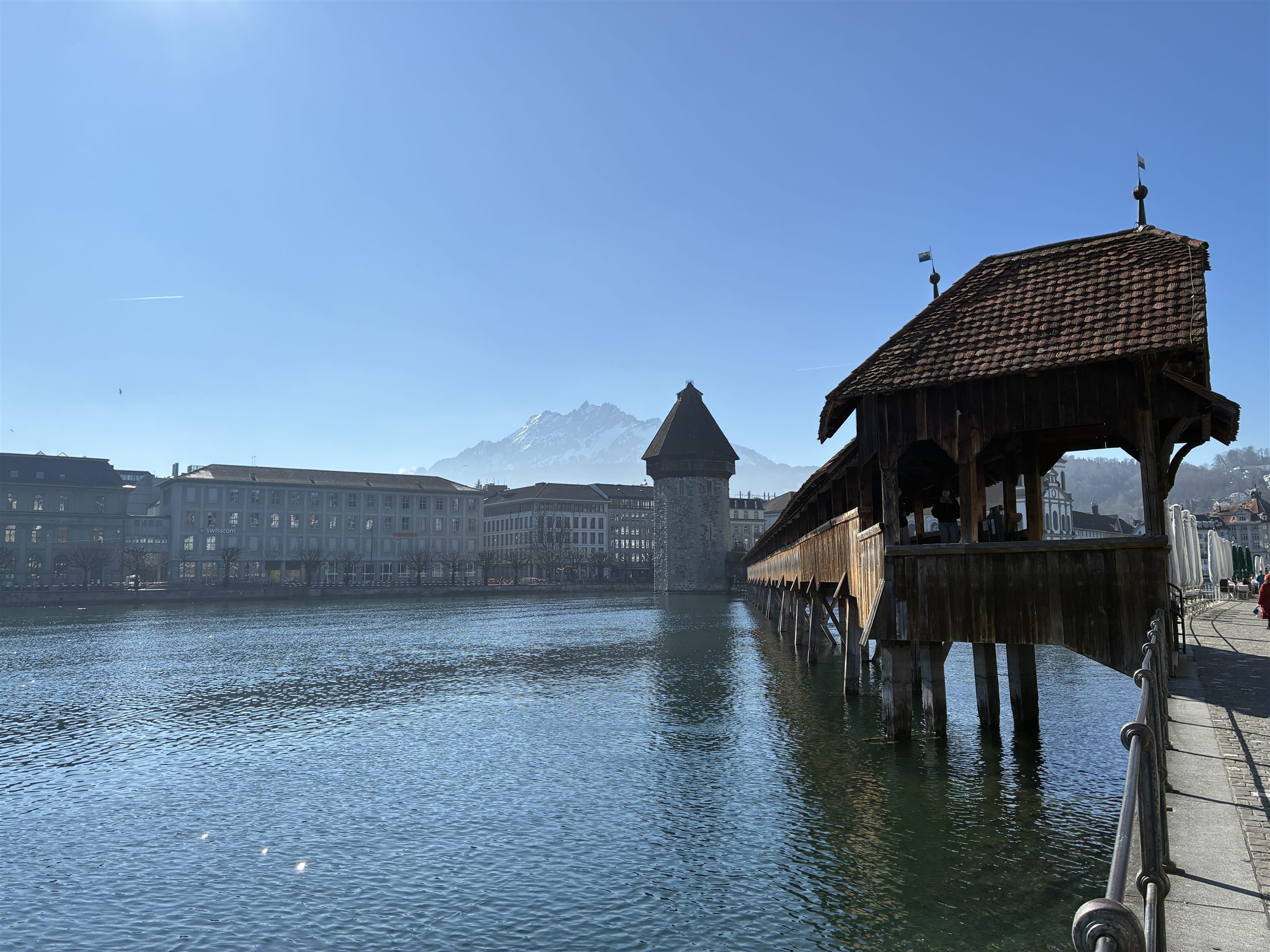 A Kapellbrücke de Lucerna vista do Reuss: a Torre d'Água octogonal, o corredor coberto de madeira, as pinturas no teto e os pilares de carvalho no rio