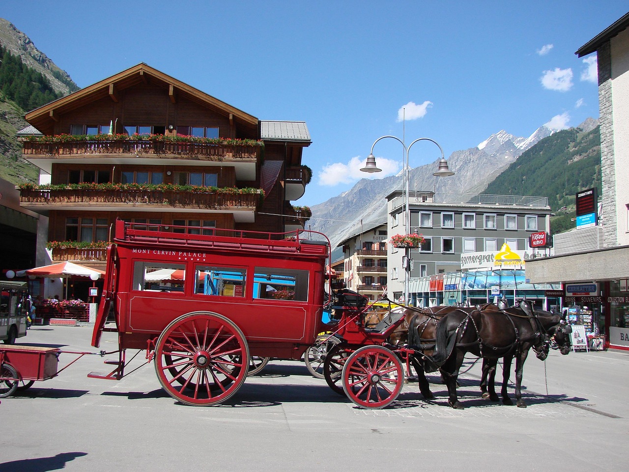 Carruagem de hotel puxada por cavalos na praça junto à estação de Zermatt, vila car-free no cantão do Valais, com as montanhas ao fundo