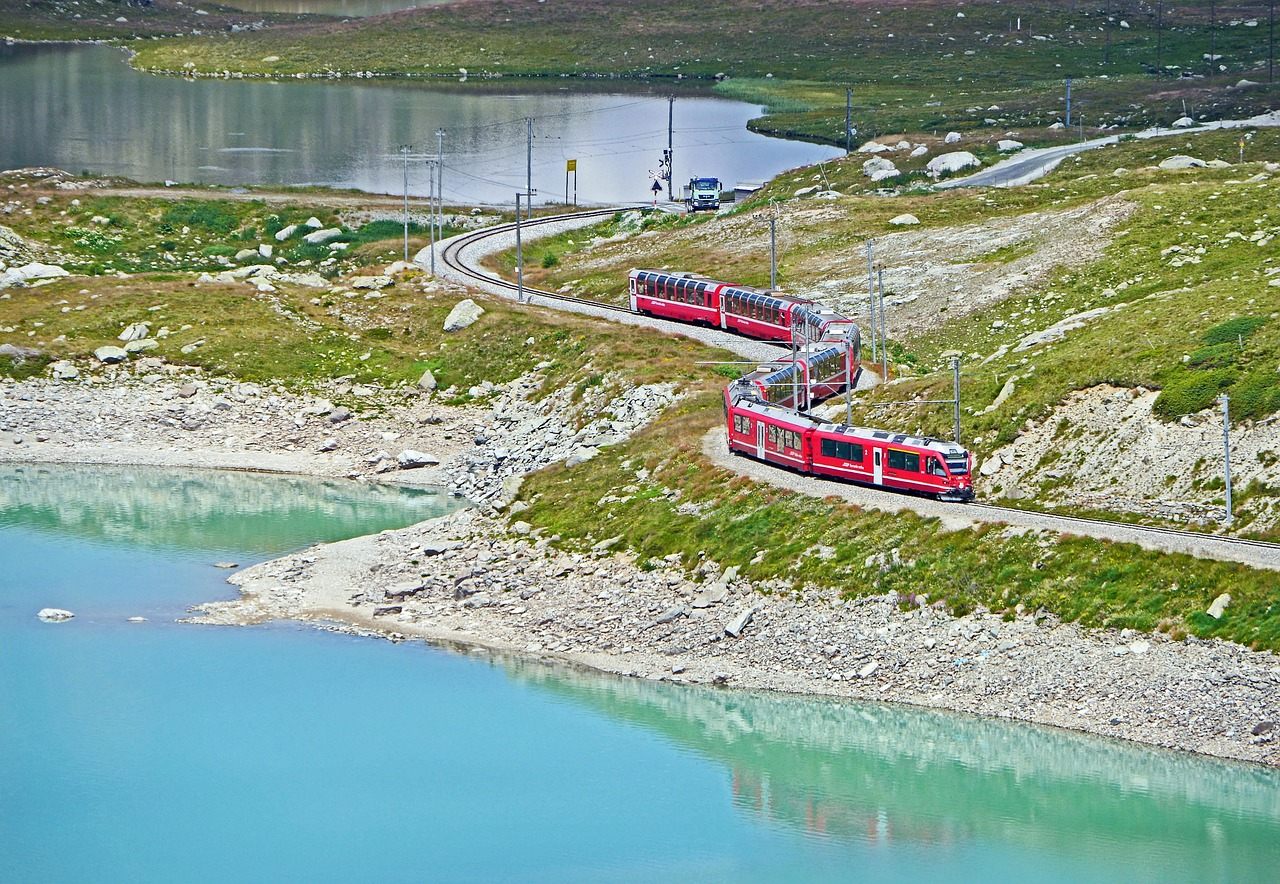Bernina Express vermelho margeando o Lago Bianco de água turquesa no ponto mais alto da travessia, nos Alpes de Graubünden