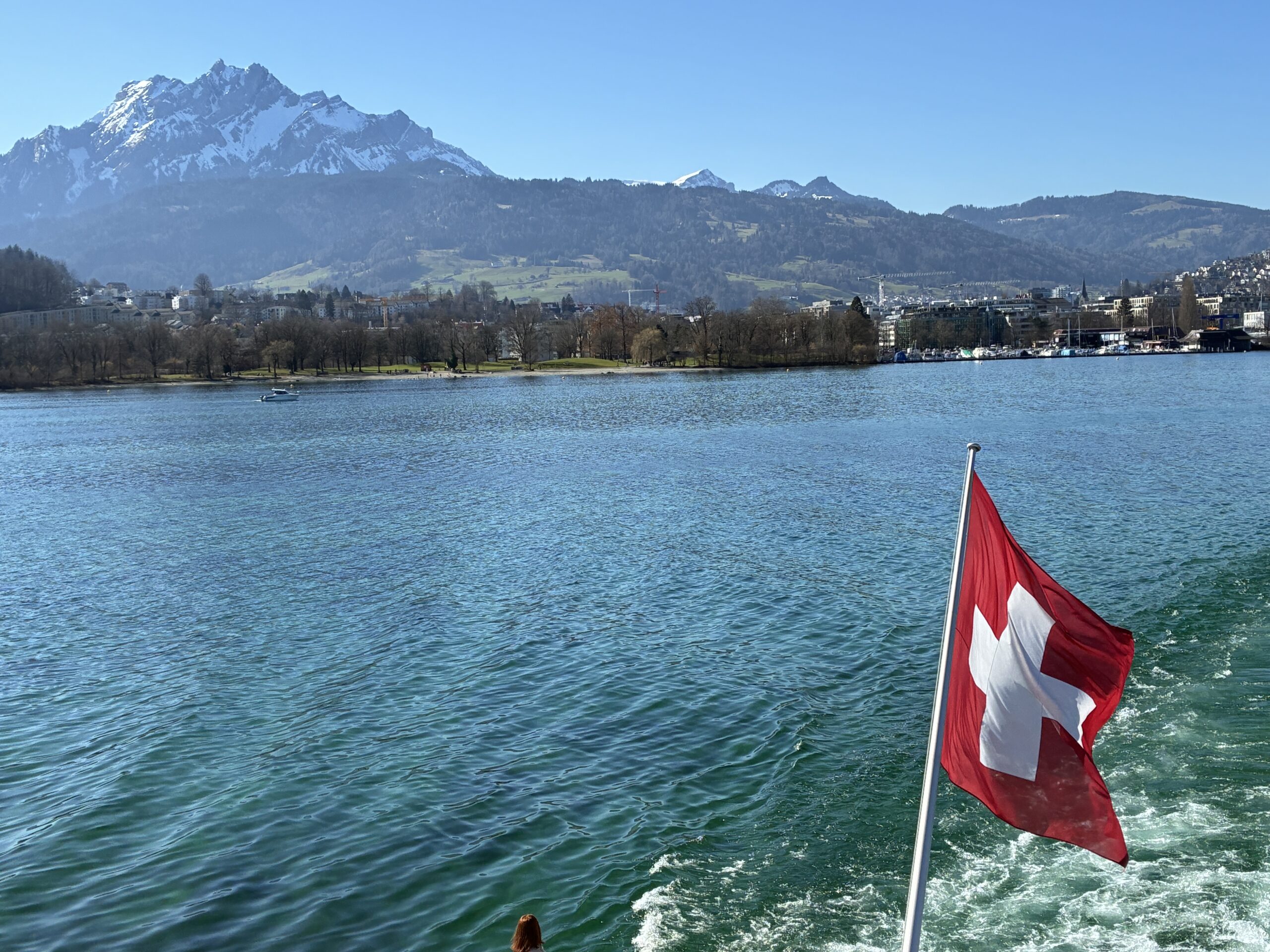 Bandeira suíça na popa de um barco de passageiros no Lago de Lucerna, com os Alpes ao fundo