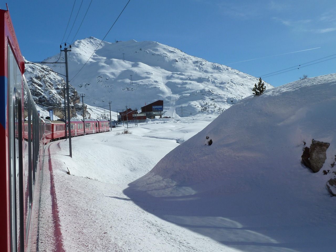 Trem panorâmico vermelho da Ferrovia Rética cruzando um passo alpino sob a neve, na Suíça