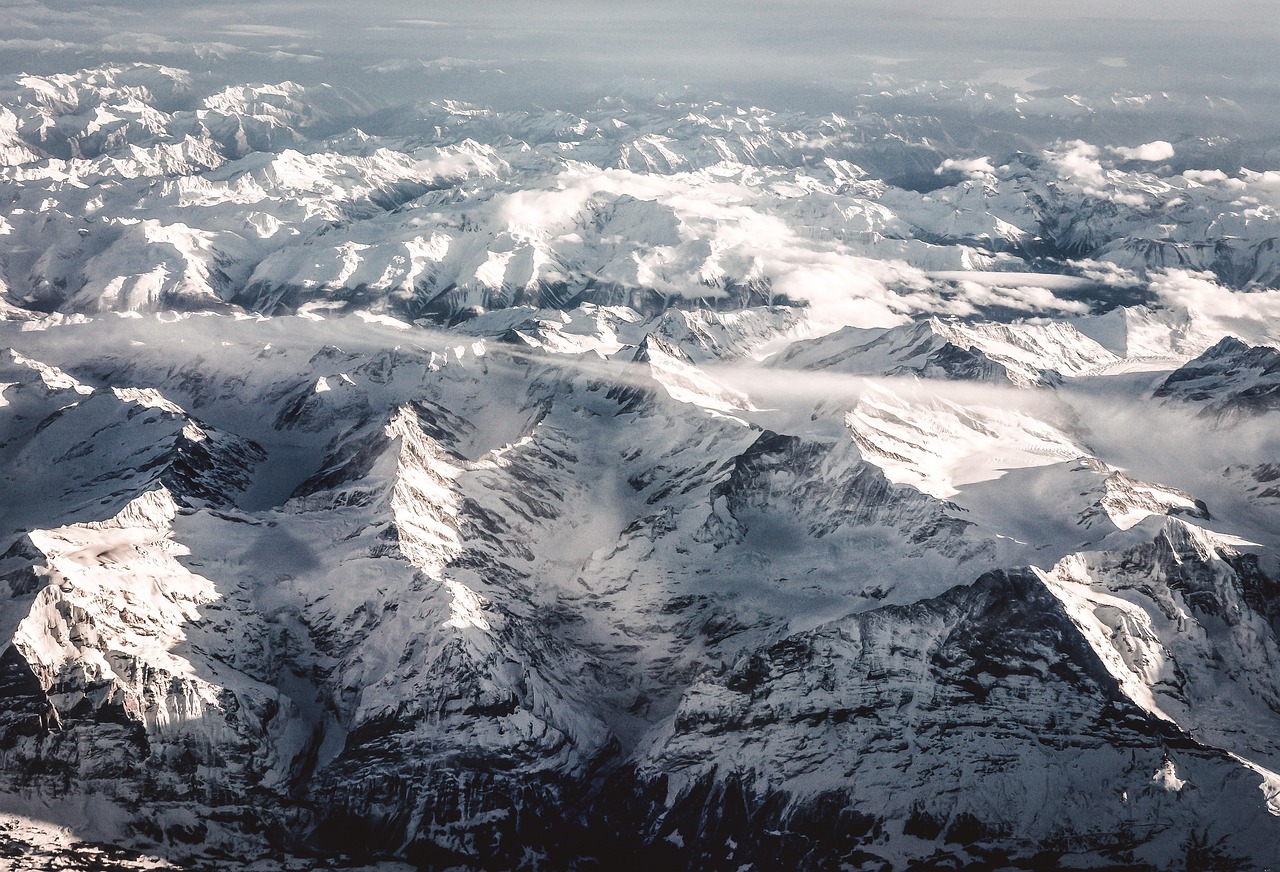 Vista aérea dos Alpes suíços cobertos de neve, picos recortados emergindo das nuvens vistos do alto