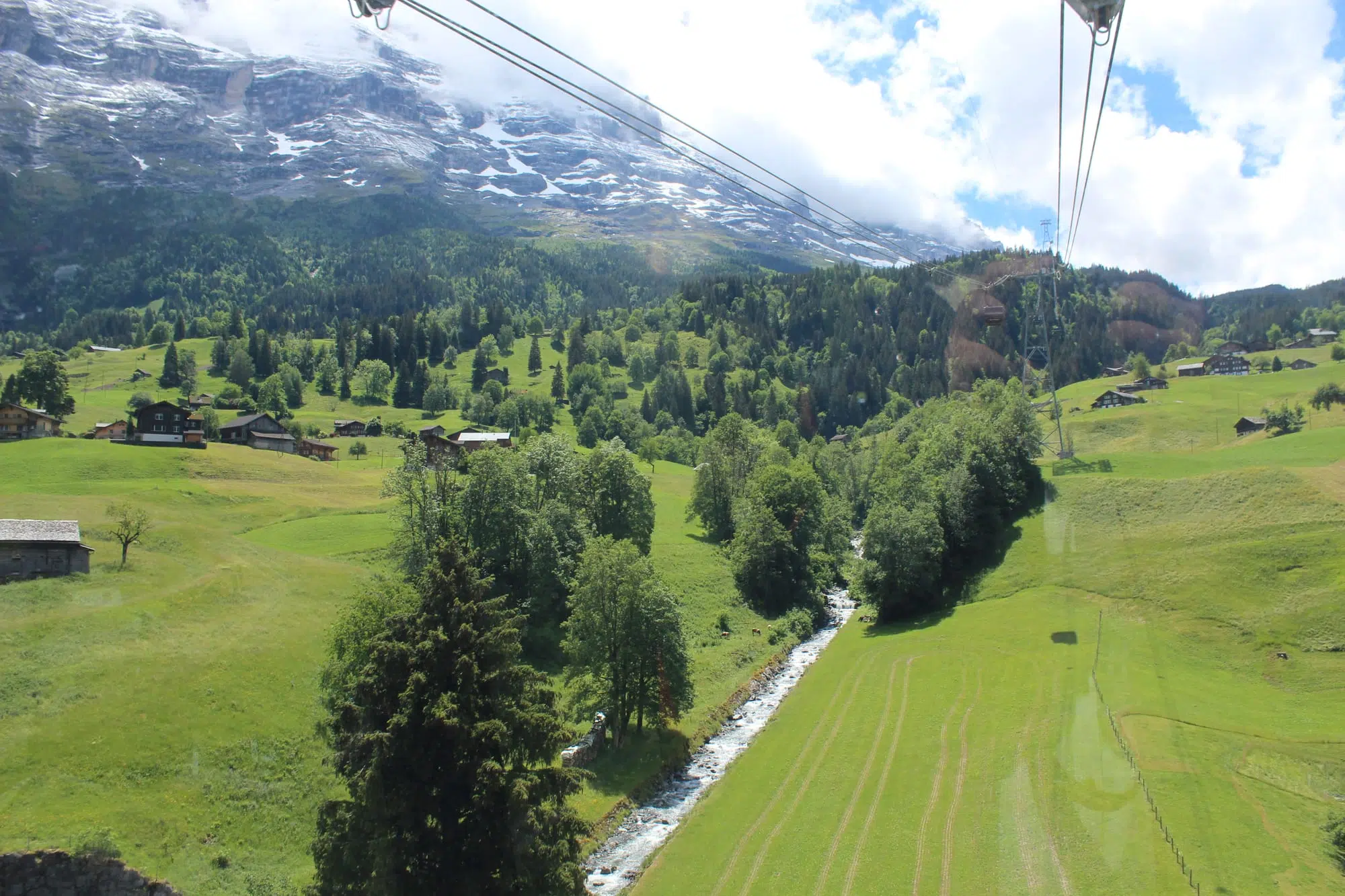Vale verde de Grindelwald com um riacho glacial e a face do Eiger ao fundo, visto de um teleférico