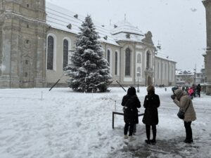A praça da abadia de São Galo sob a neve, com uma árvore nevada e flocos caindo