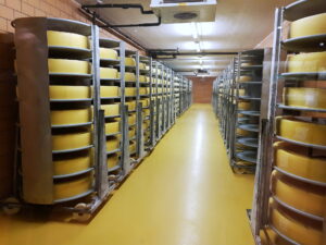 Corredor da cave de maturação da Emmentaler Schaukäserei, com rodas de queijo nos carros de prateleira dos dois lados