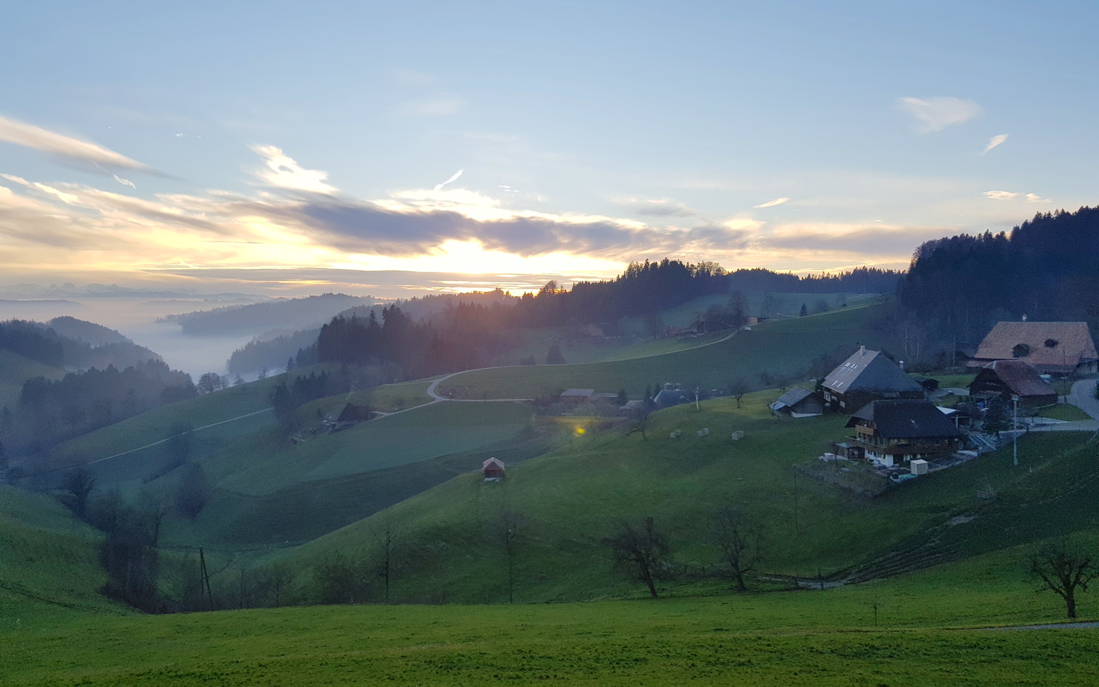 Colinas verdes do Emmental ao entardecer, com névoa no fundo do vale e fazendas de telhado largo