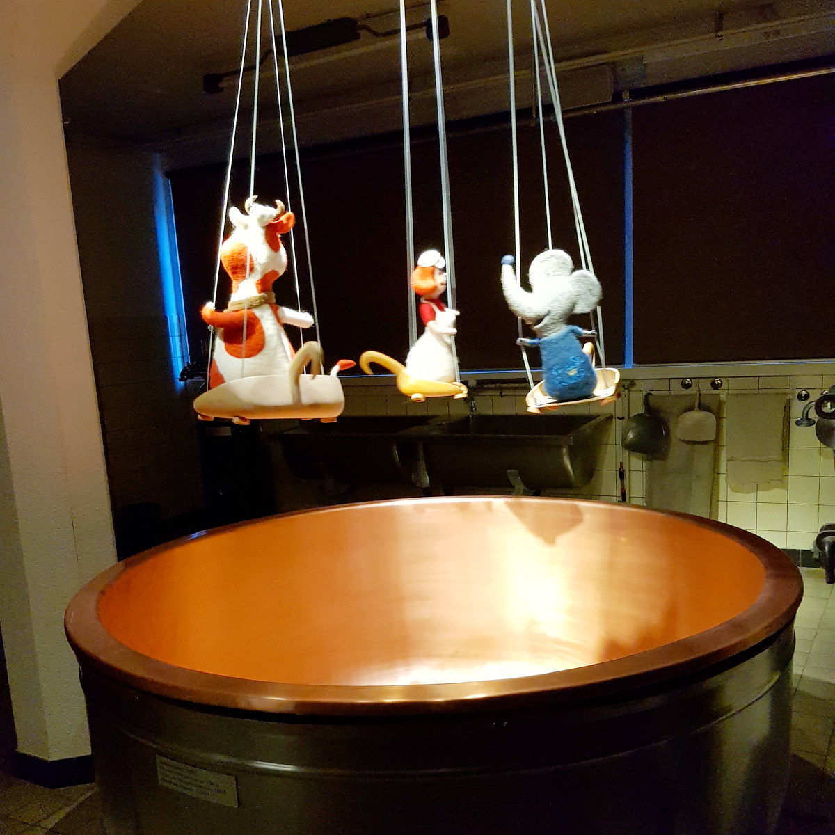 Tacho de cobre da queijaria com marionetes de feltro de vaca, queijeiro e rato penduradas por cima