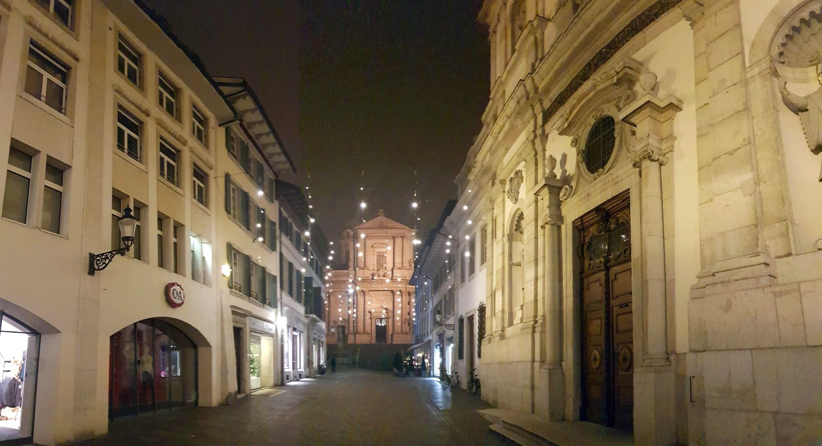 Viela da cidade velha de Solothurn à noite, com luzes de Advento suspensas e uma fachada barroca iluminada ao fundo