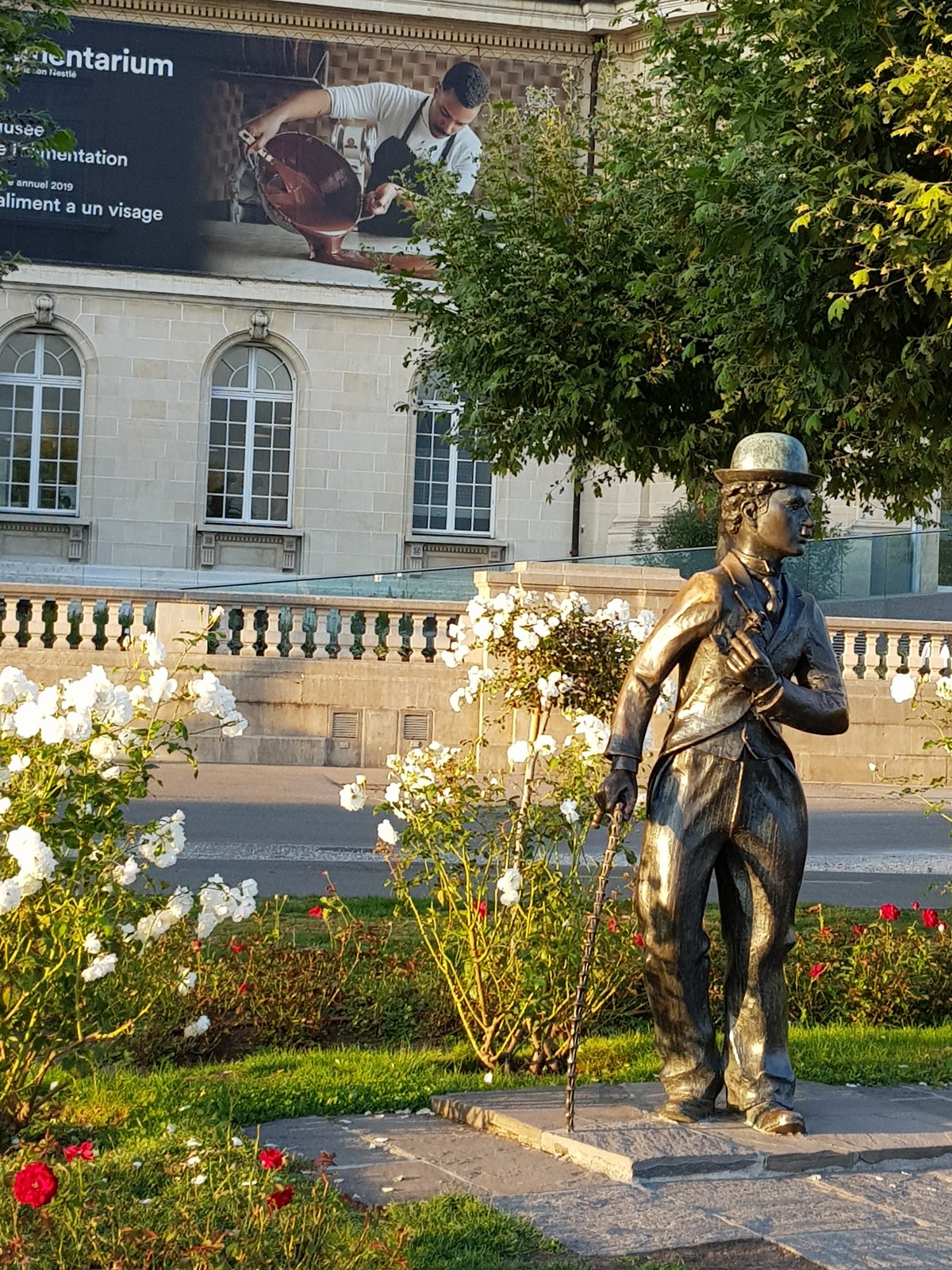 Estátua de Charlie Chaplin em bronze na orla de Vevey, com roseiral e o prédio do Alimentarium ao fundo
