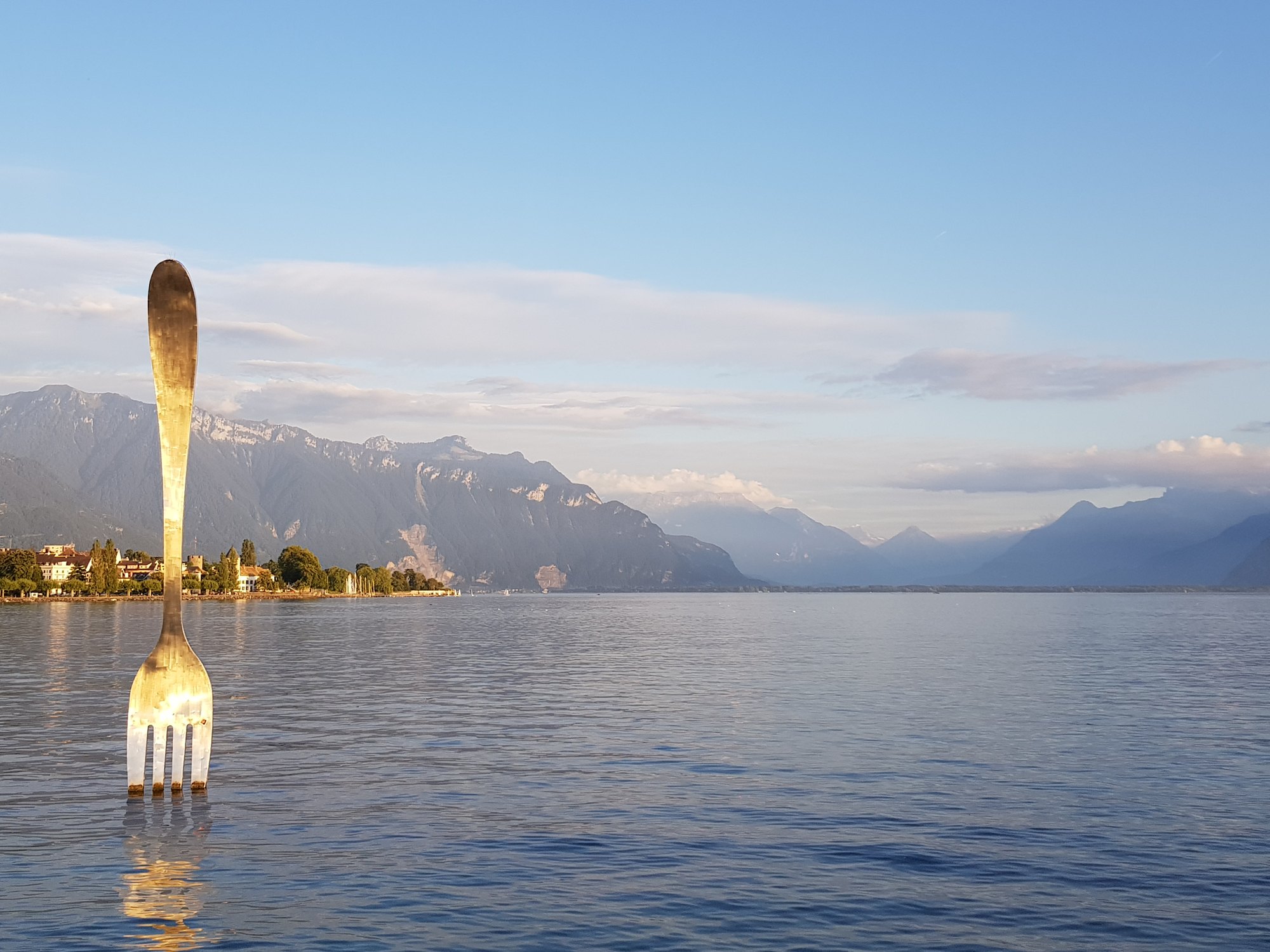 O garfo gigante de Vevey fincado no Lago Léman ao entardecer, com os Alpes ao fundo