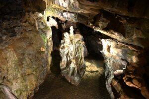 Salão das Grutas de São Beatus com coluna de calcita iluminada sobre uma lâmina de água