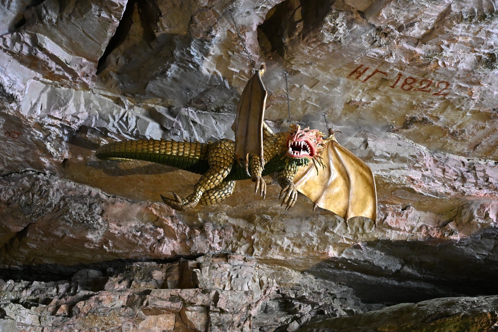 Escultura de dragão presa por correntes na parede das Grutas de São Beatus, ao lado da inscrição vermelha de 1822