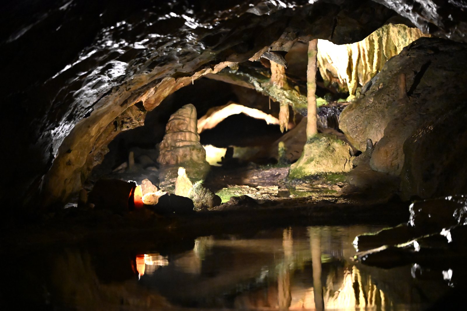 Lago subterrâneo dentro das Grutas de São Beatus com uma coluna de calcita e luz alaranjada refletida na água parada