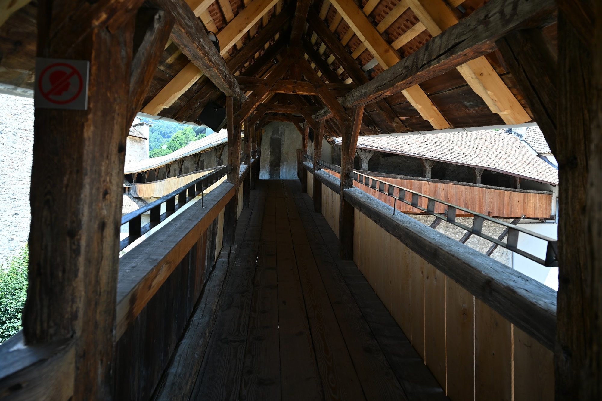 Adarve de madeira do Castelo de Chillon com corrimão de tábuas e uma segunda galeria coberta do outro lado, sobre os telhados