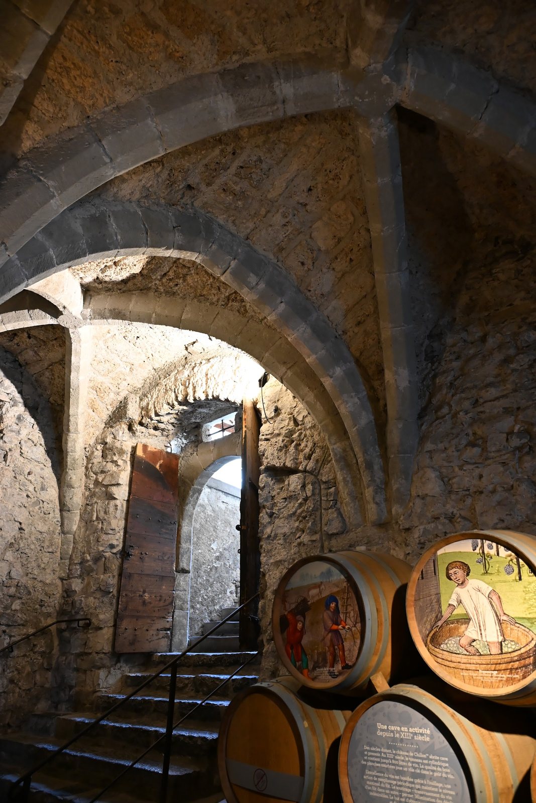 Escada de pedra e porta medieval na entrada da adega do Castelo de Chillon, com barris de topo pintado à direita