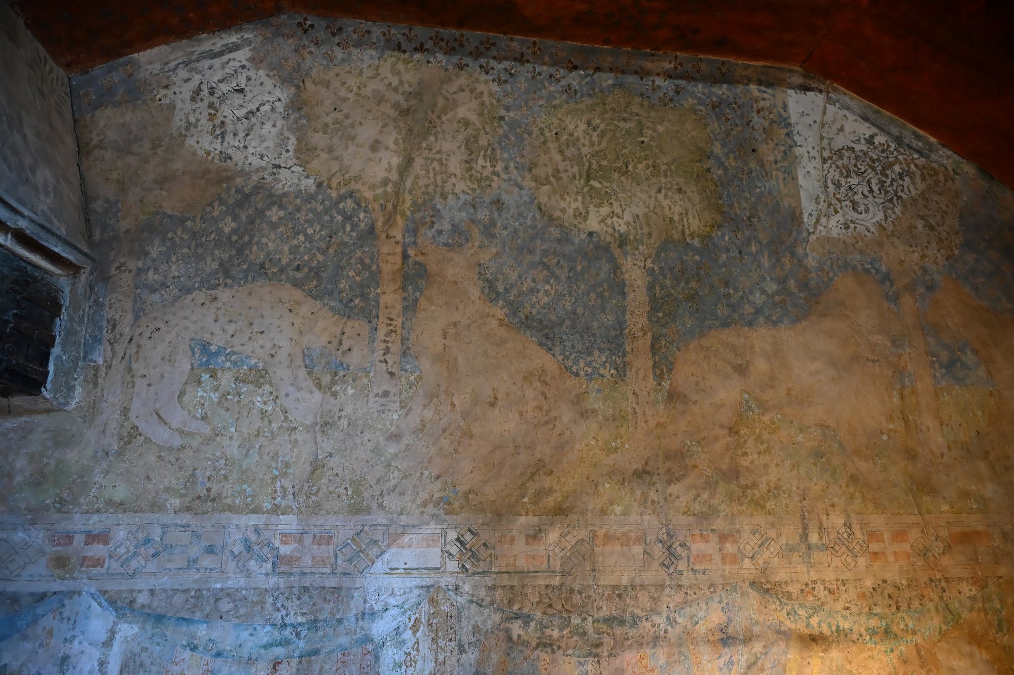 Pintura mural do século XIV na camera domini do Castelo de Chillon, com animais entre árvores sobre fundo de flores-de-lis