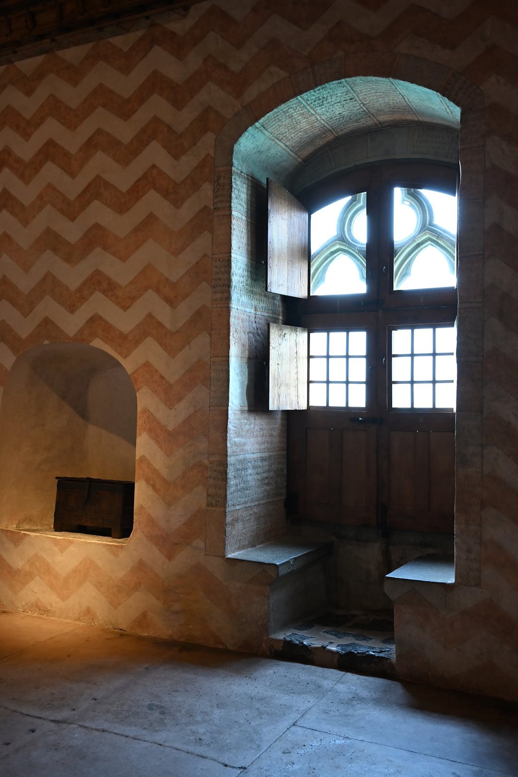 Janela gótica do Castelo de Chillon com bancos de pedra e parede pintada em chevrons alaranjados