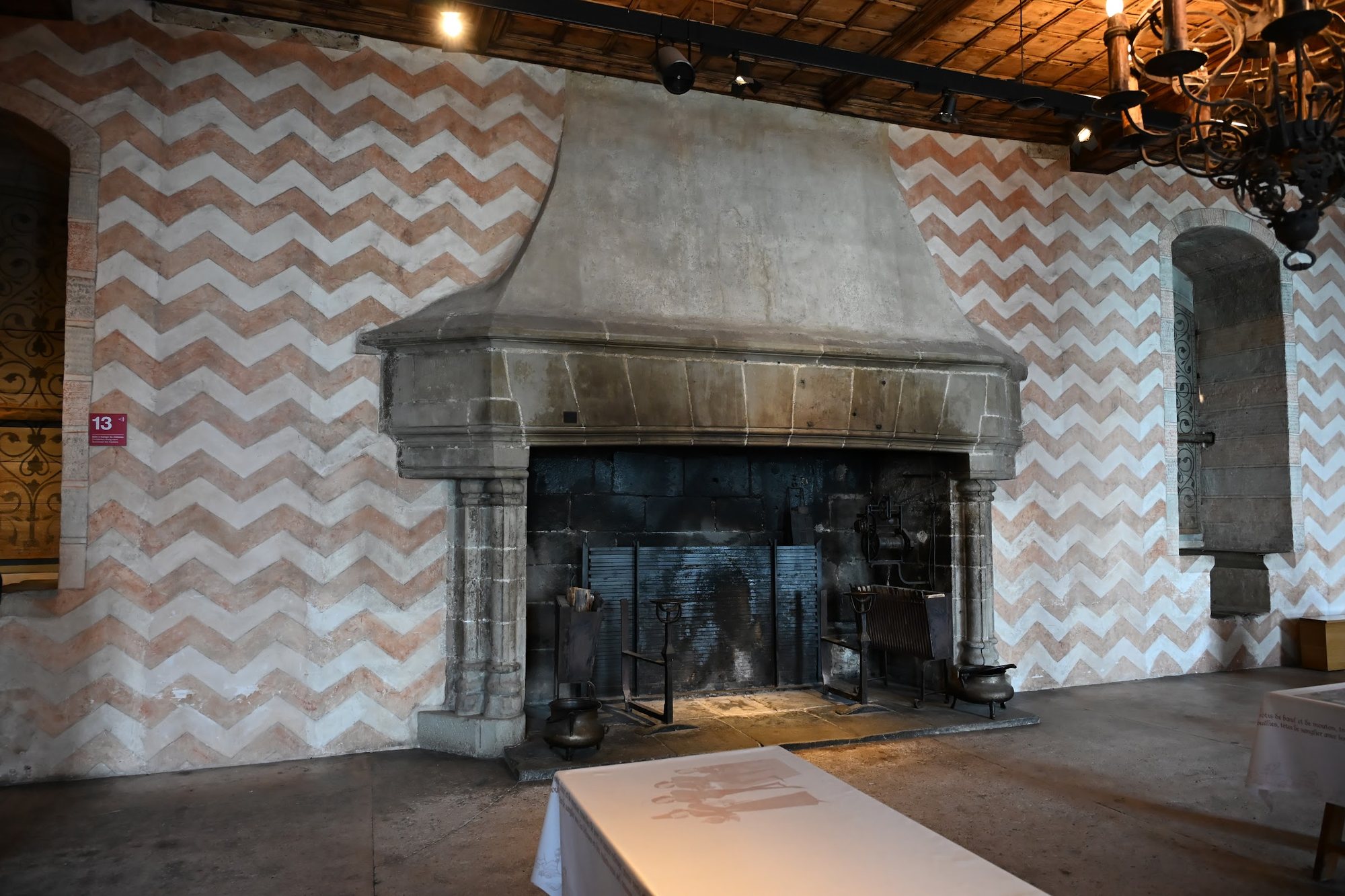 Lareira monumental da sala de jantar do castelão em Chillon, com as paredes pintadas em chevrons e a placa da sala 13
