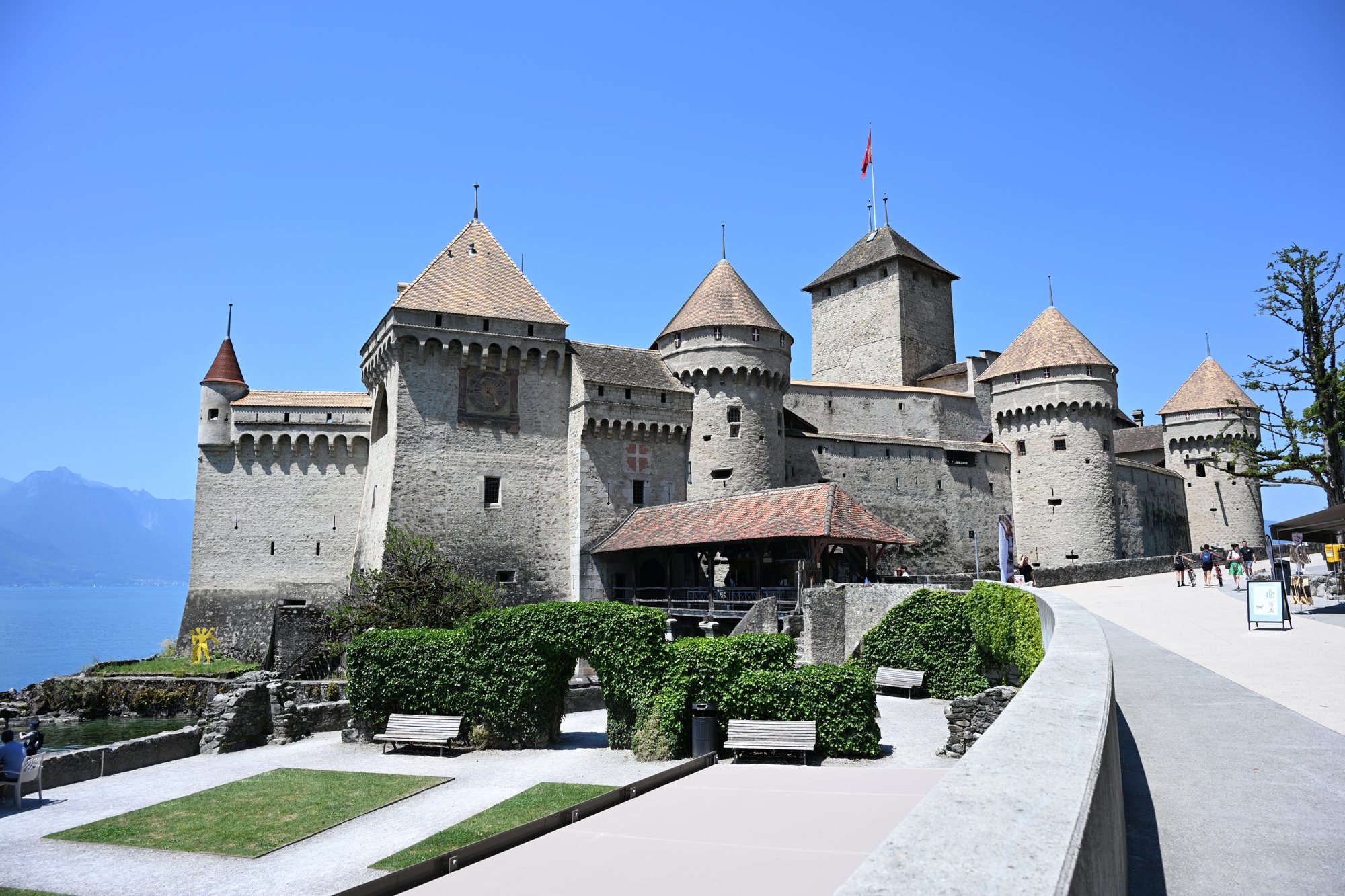 Entrada do Castelo de Chillon com o jardim, a ponte coberta e as torres redondas sob céu azul