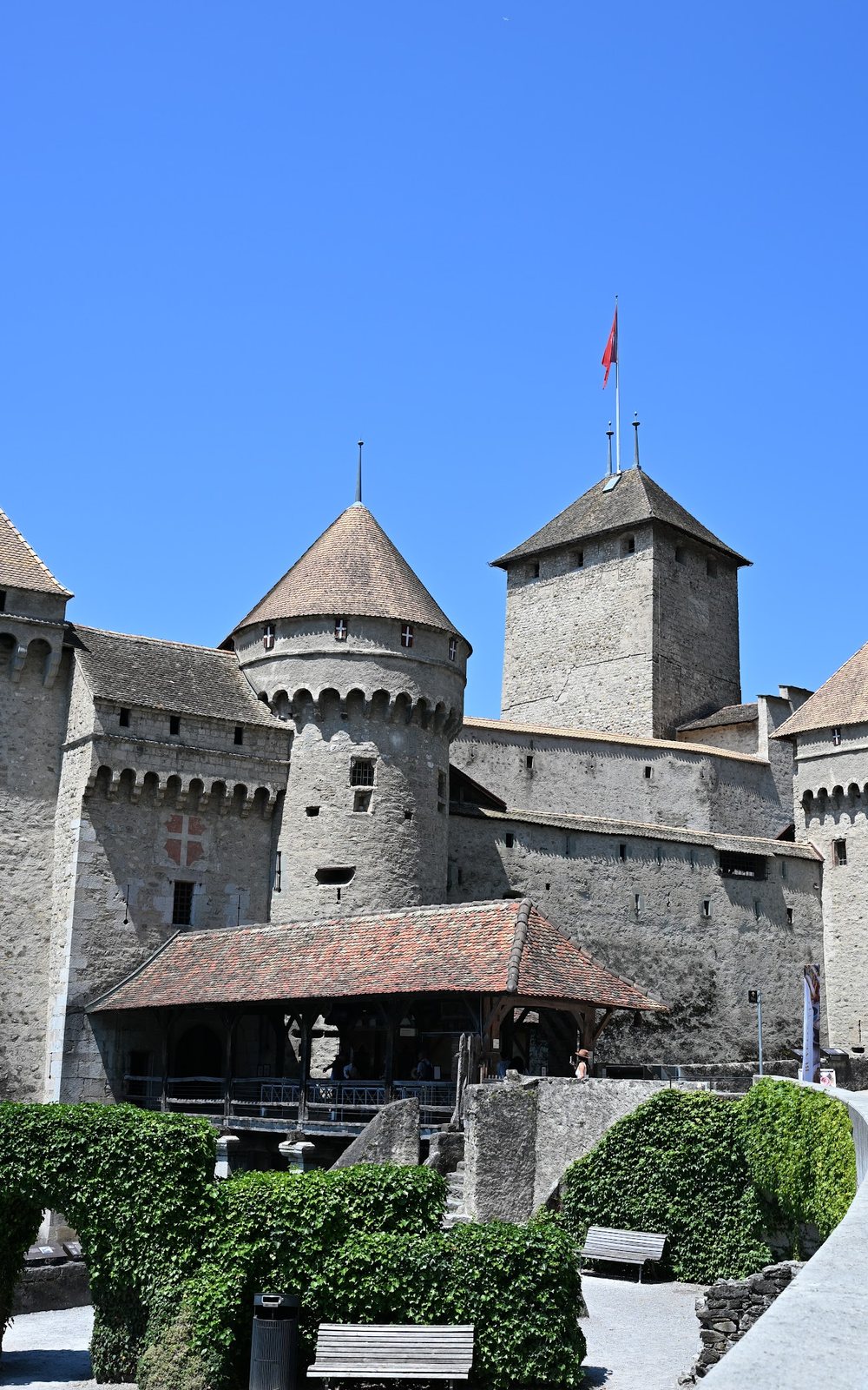 Fachada do Castelo de Chillon voltada para a terra, com duas torres redondas de matacães, a torre de menagem quadrada ao fundo e a galeria de madeira sobre a entrada