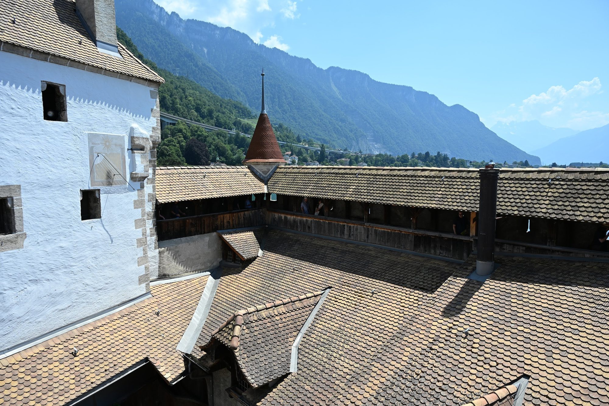 Vista do alto do Castelo de Chillon com as galerias de madeira cobertas correndo em volta do pátio, telhados de escamas de barro e as montanhas do outro lado do lago