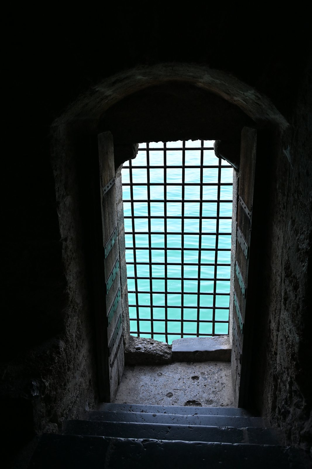 Grade de ferro numa abertura da prisão de Chillon com a água turquesa do Lago Léman do lado de fora