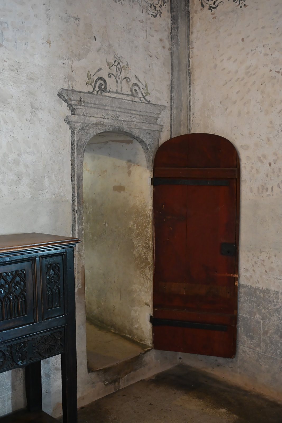 Nicho pintado no Castelo de Chillon com moldura em grisalha e ornamento de flor-de-lis no topo, ao lado de uma porta vermelha