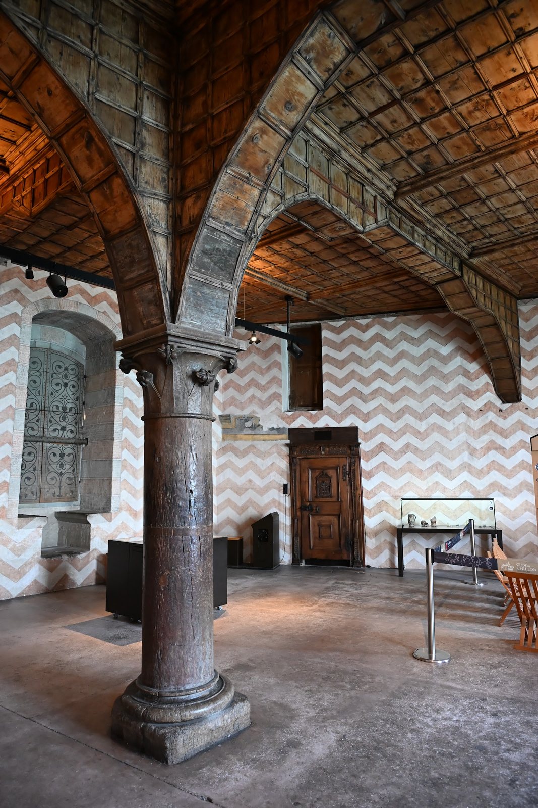 Grande sala do Castelo de Chillon com coluna de carvalho, arcos de madeira e paredes pintadas em chevrons de ocre e branco