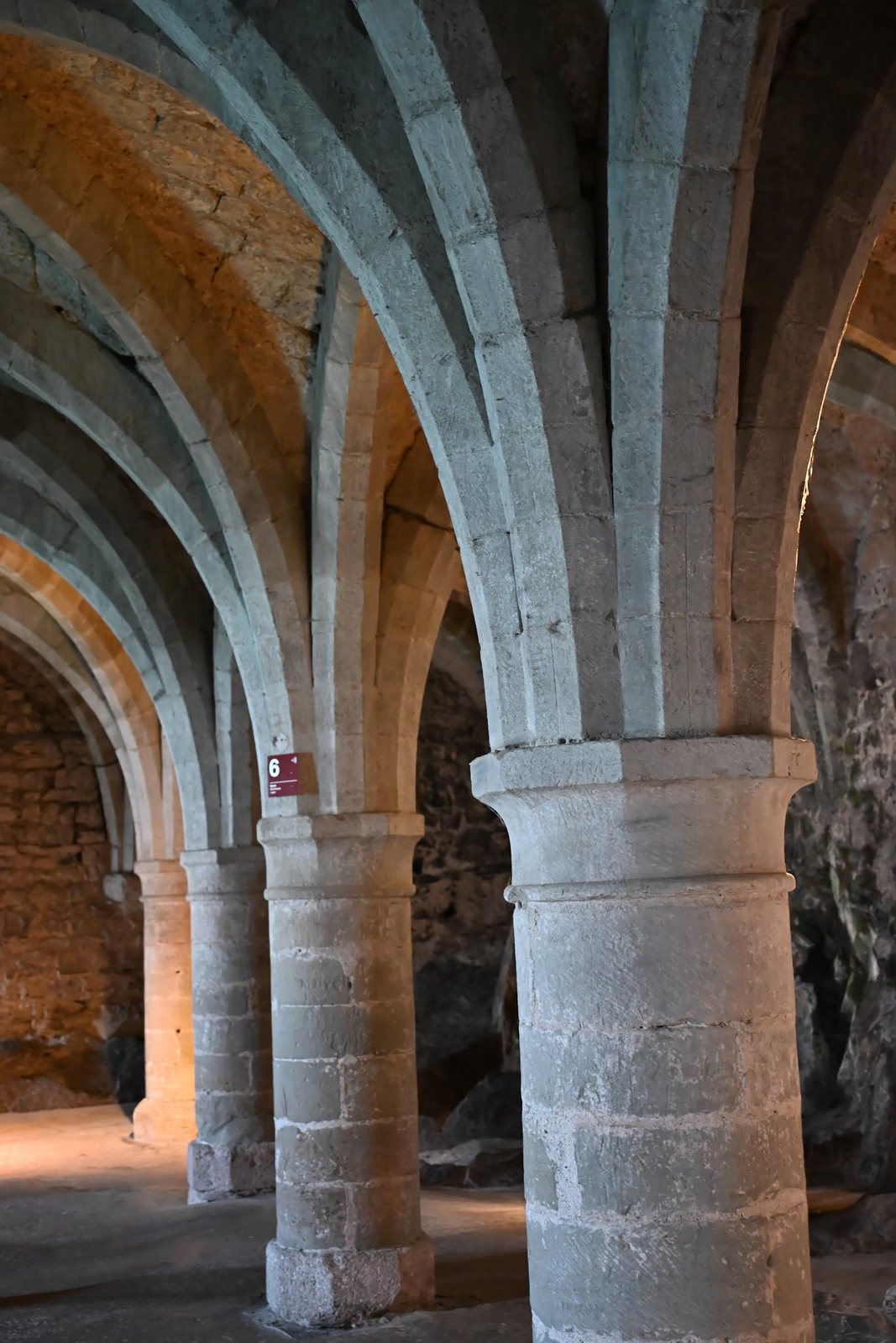 Pilares e abóbadas góticas dos subterrâneos do Castelo de Chillon, com a placa da sala 6 na coluna