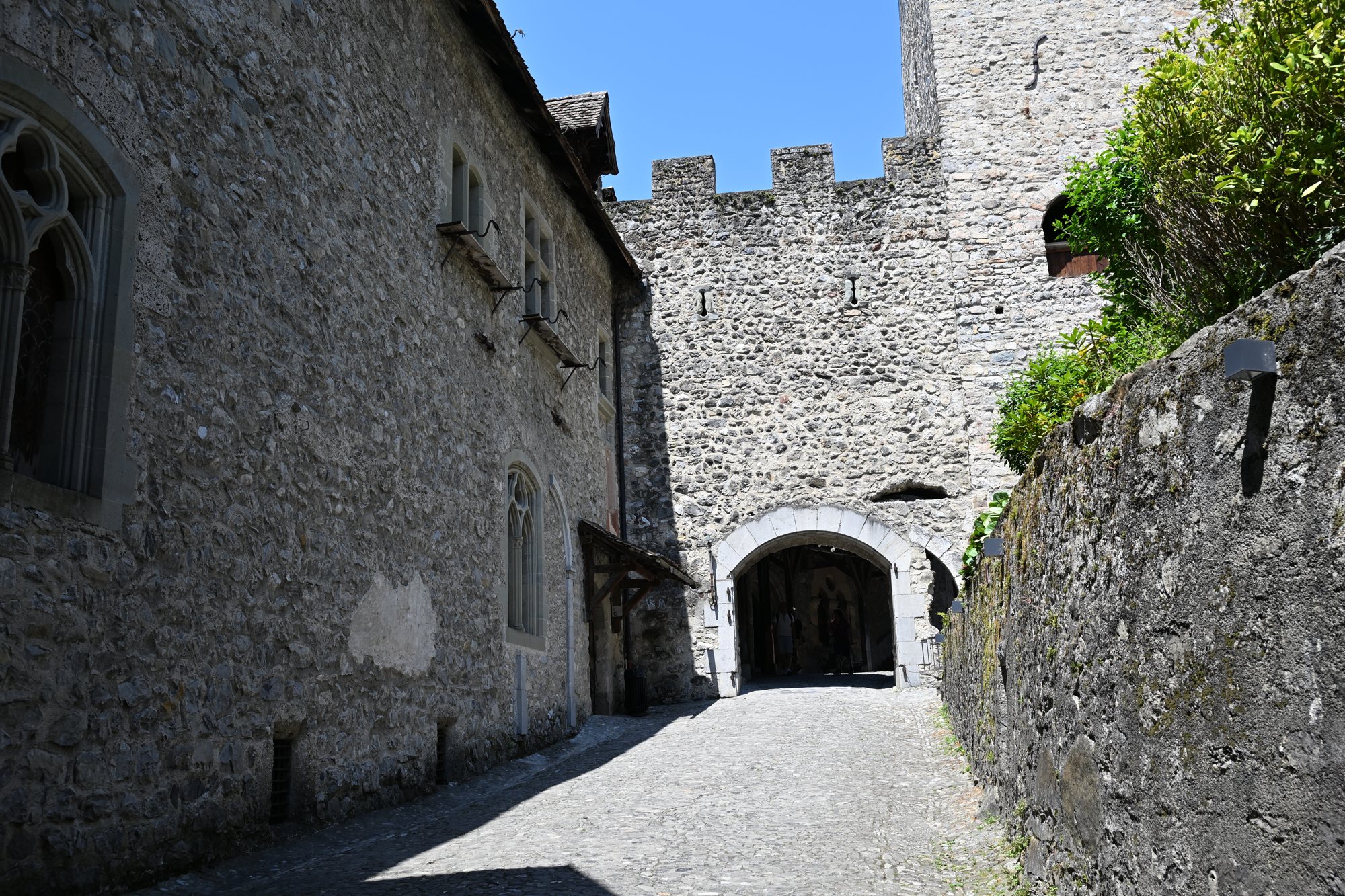 Ruela de pedra dentro do Castelo de Chillon com janela gótica, muralha ameada e passagem em arco