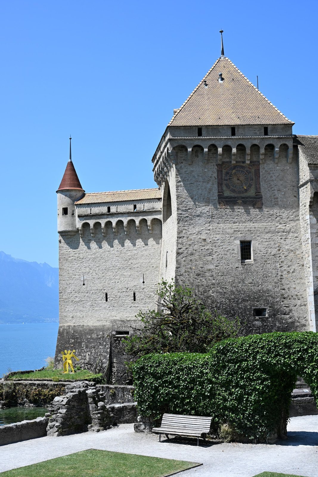 Torre do relógio do Castelo de Chillon com o mostrador pintado na pedra e um torreão de telhado vermelho ao lado