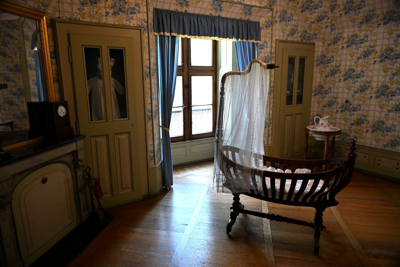 Berço com dossel de renda em quarto de papel de parede florido no Castelo de Oberhofen