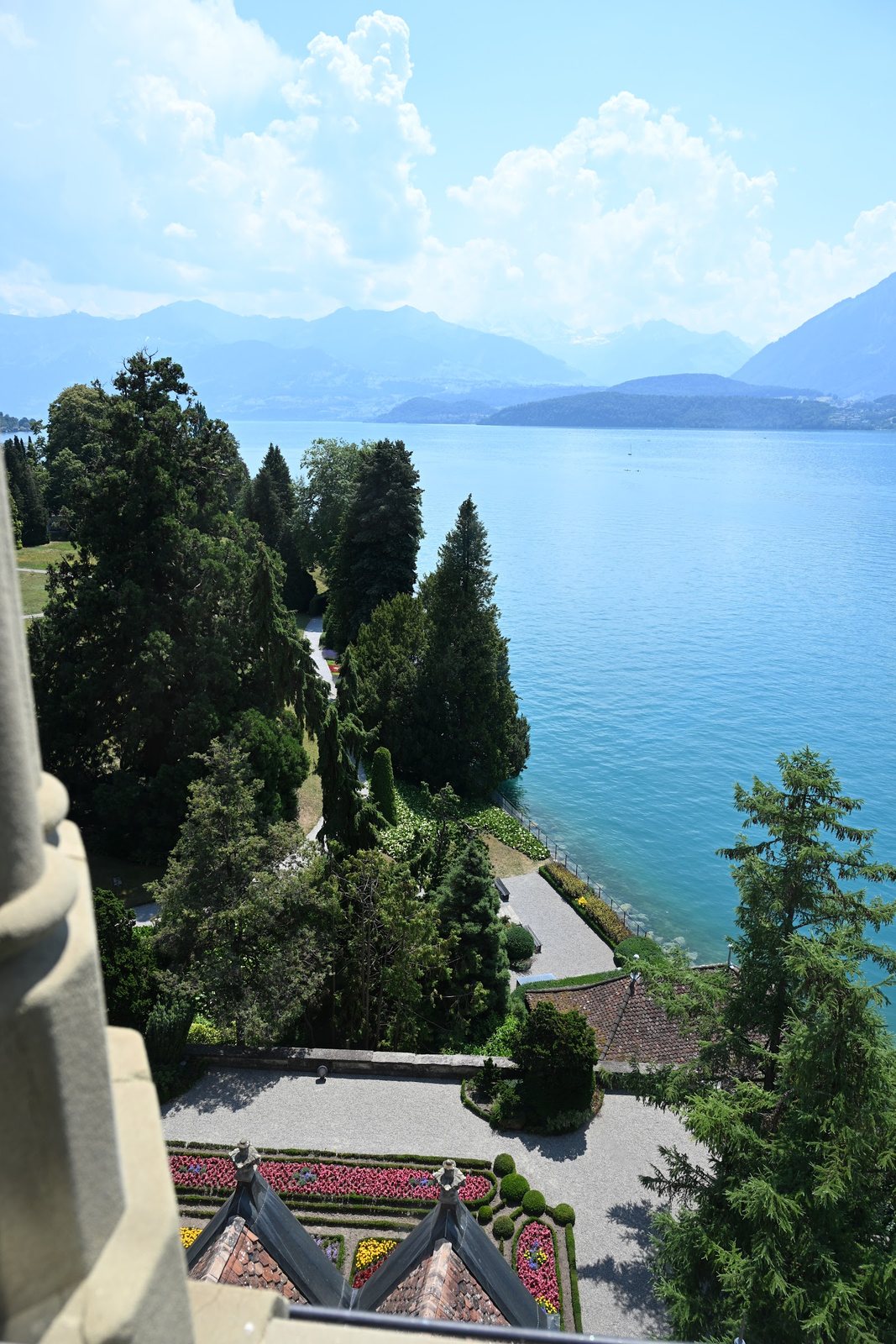 Parque do Castelo de Oberhofen descendo entre árvores até a margem do Lago Thun, com montanhas ao fundo