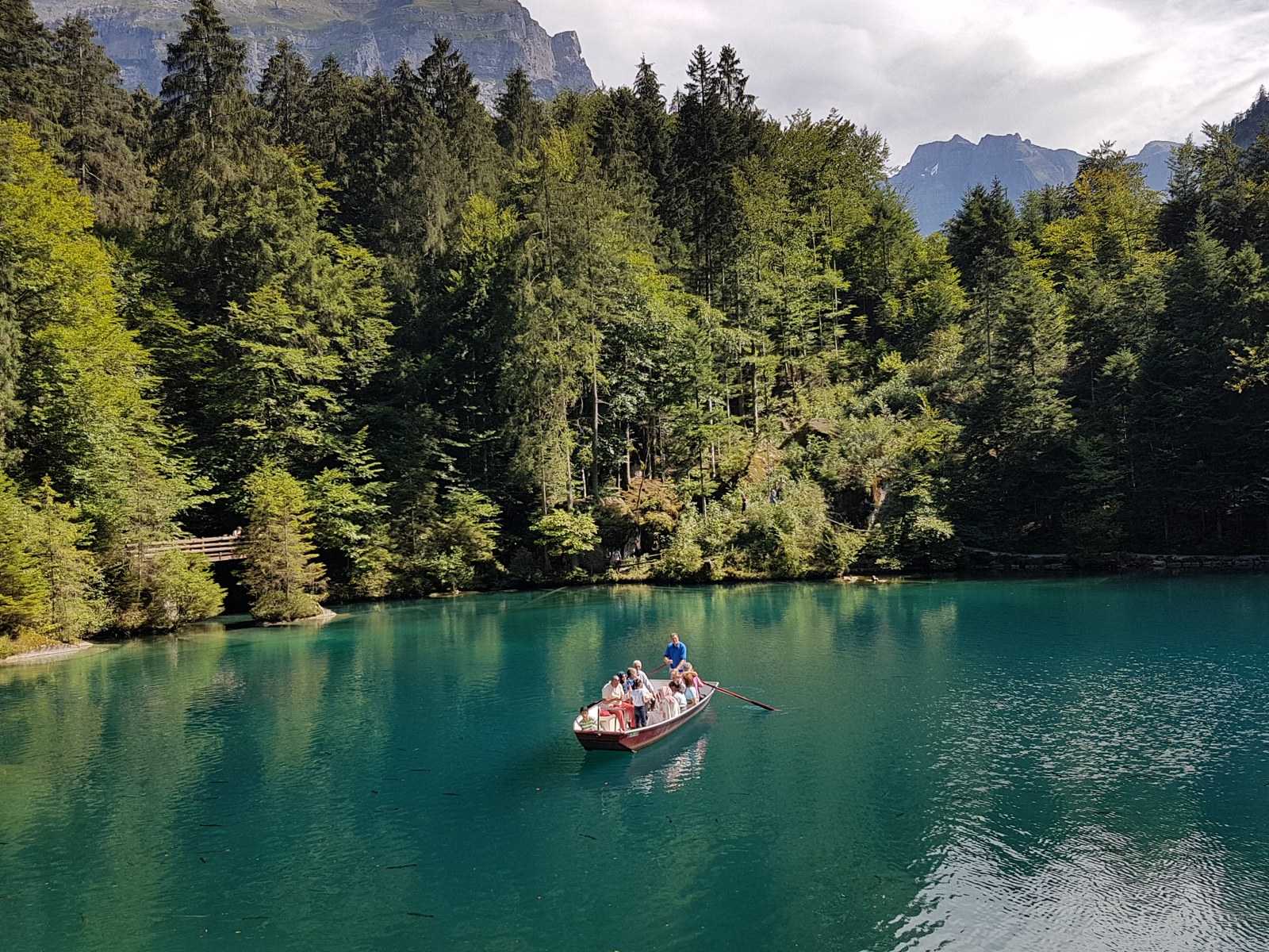 Água azul do Blausee, barco de passeio e floresta no Oberland Bernês
