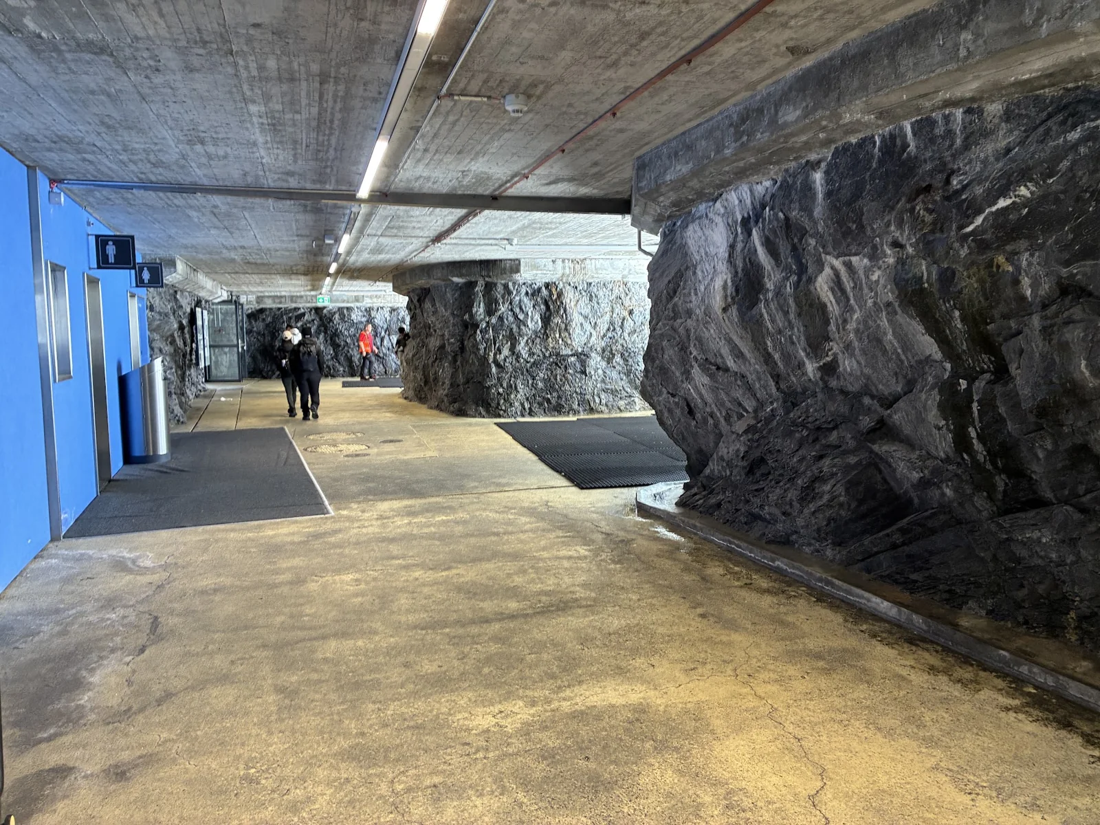 Corredor com paredes de rocha aparente, iluminação no teto e visitantes ao fundo