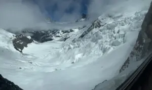 Geleira coberta de neve e paredões rochosos vistos através de uma janela