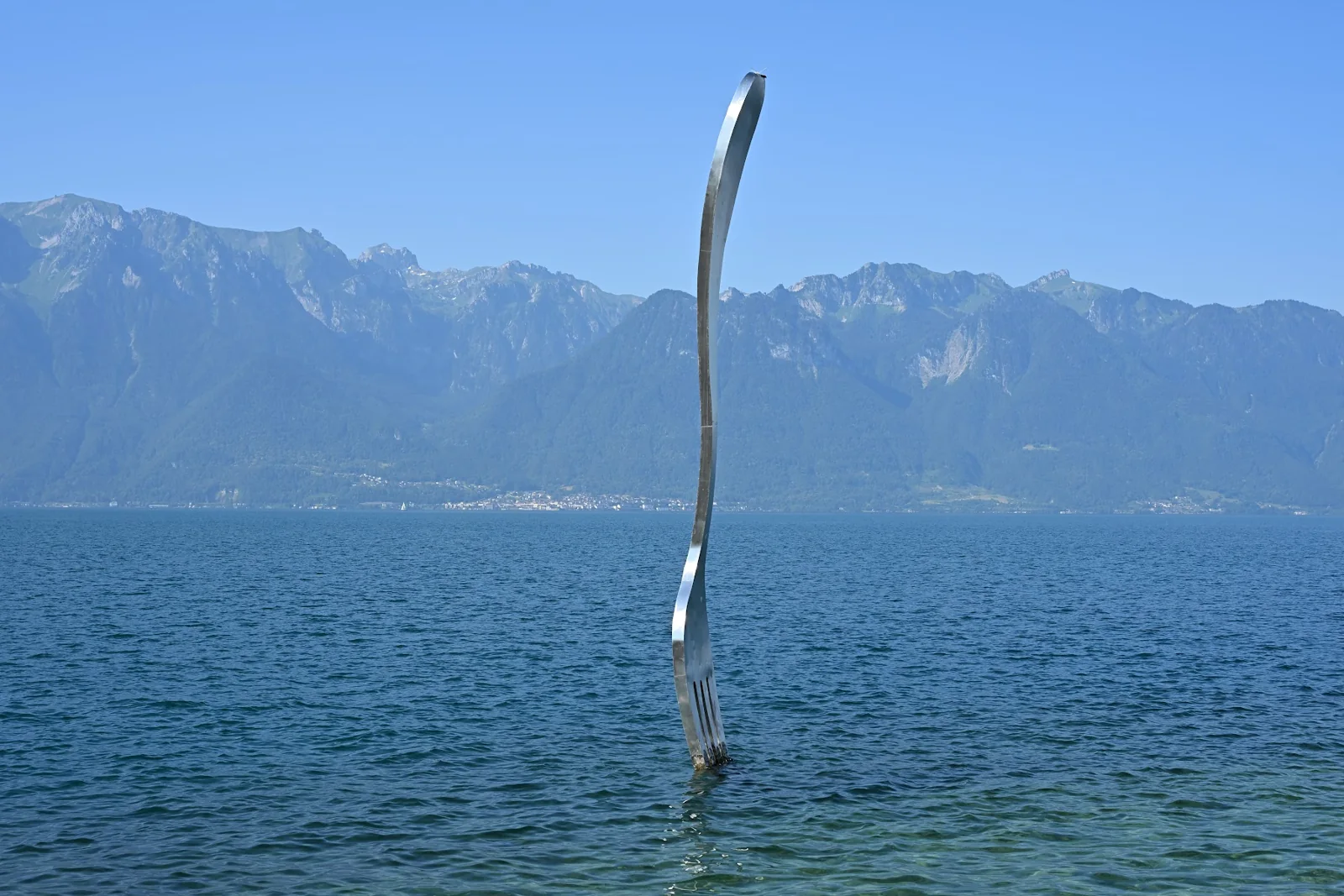Escultura de um garfo no Lago Léman, em Vevey, com montanhas ao fundo