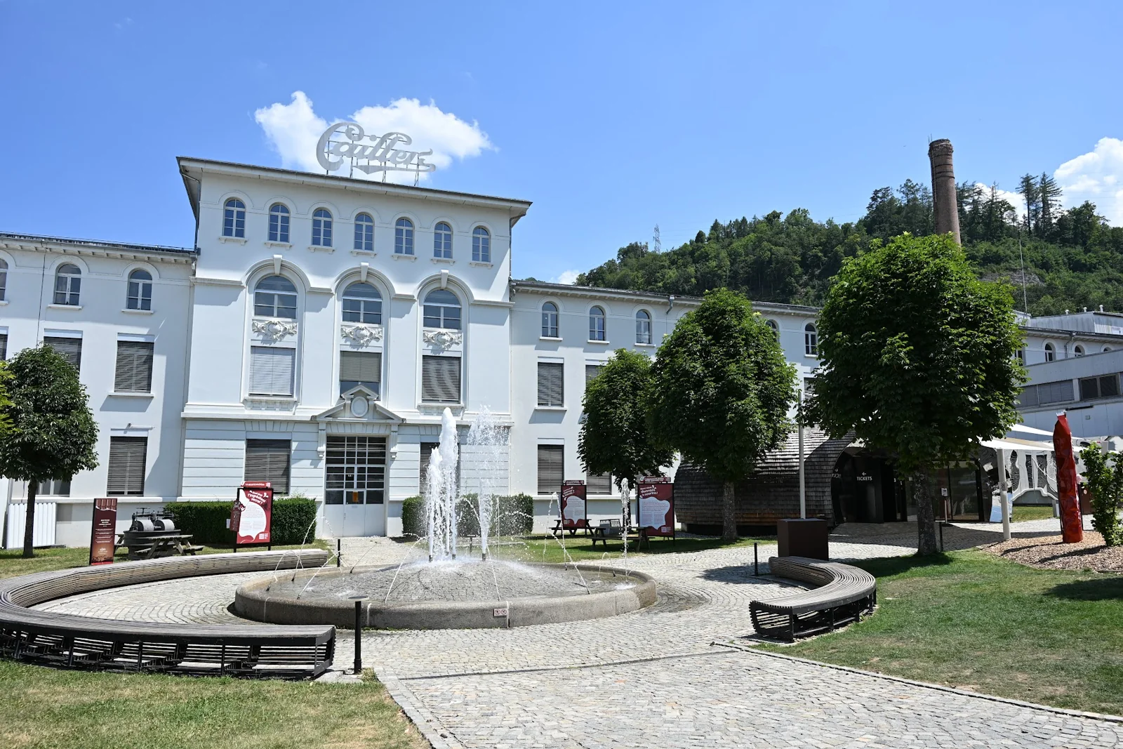 Fachada branca da Maison Cailler, em Broc, com fonte e jardim