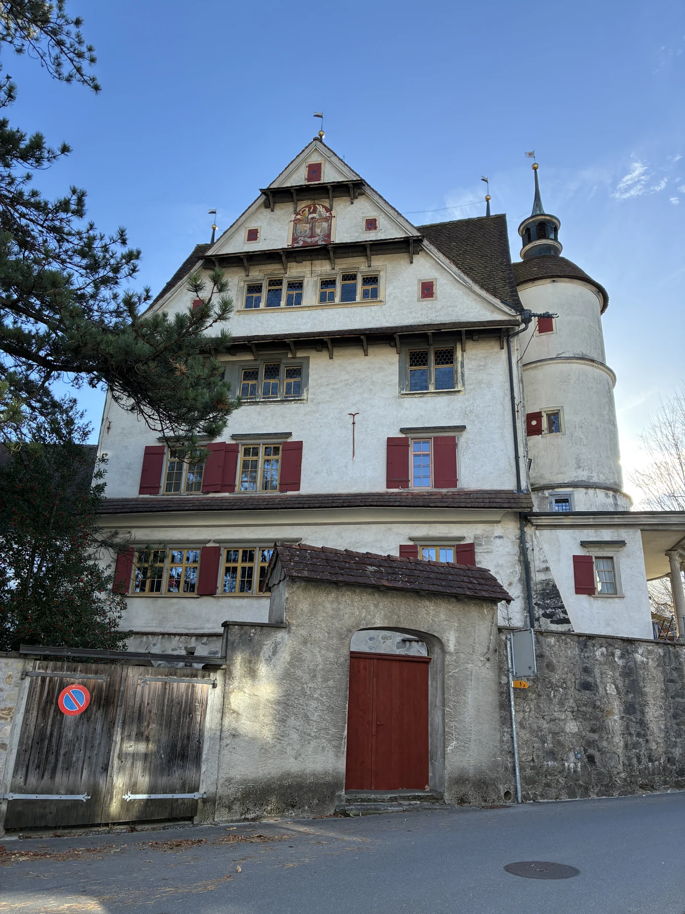 Edifício de fachada clara, torre arredondada e janelas com venezianas vermelhas em Appenzell