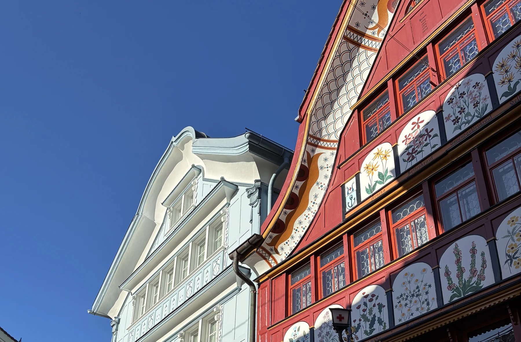 Fachadas clara e vermelha com painéis florais pintados na Hauptgasse de Appenzell