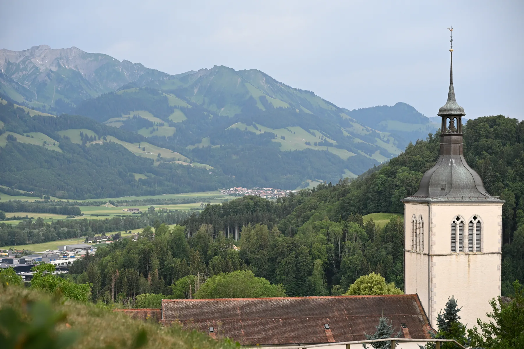 Torre da igreja de Gruyères diante de colinas e pastagens
