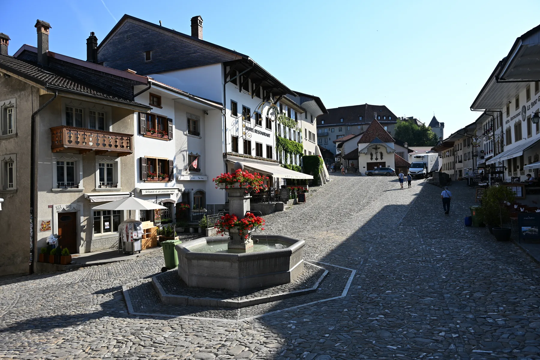 Rua principal de Gruyères com fonte, fachadas e pavimento de pedra