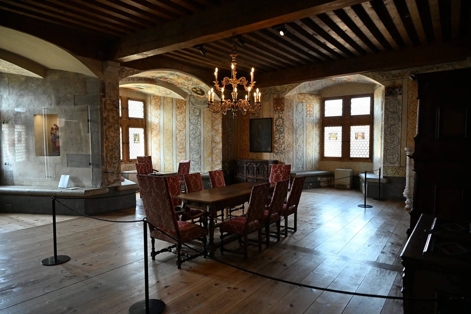 Sala do castelo com mesa de madeira, cadeiras, pilares e lustre