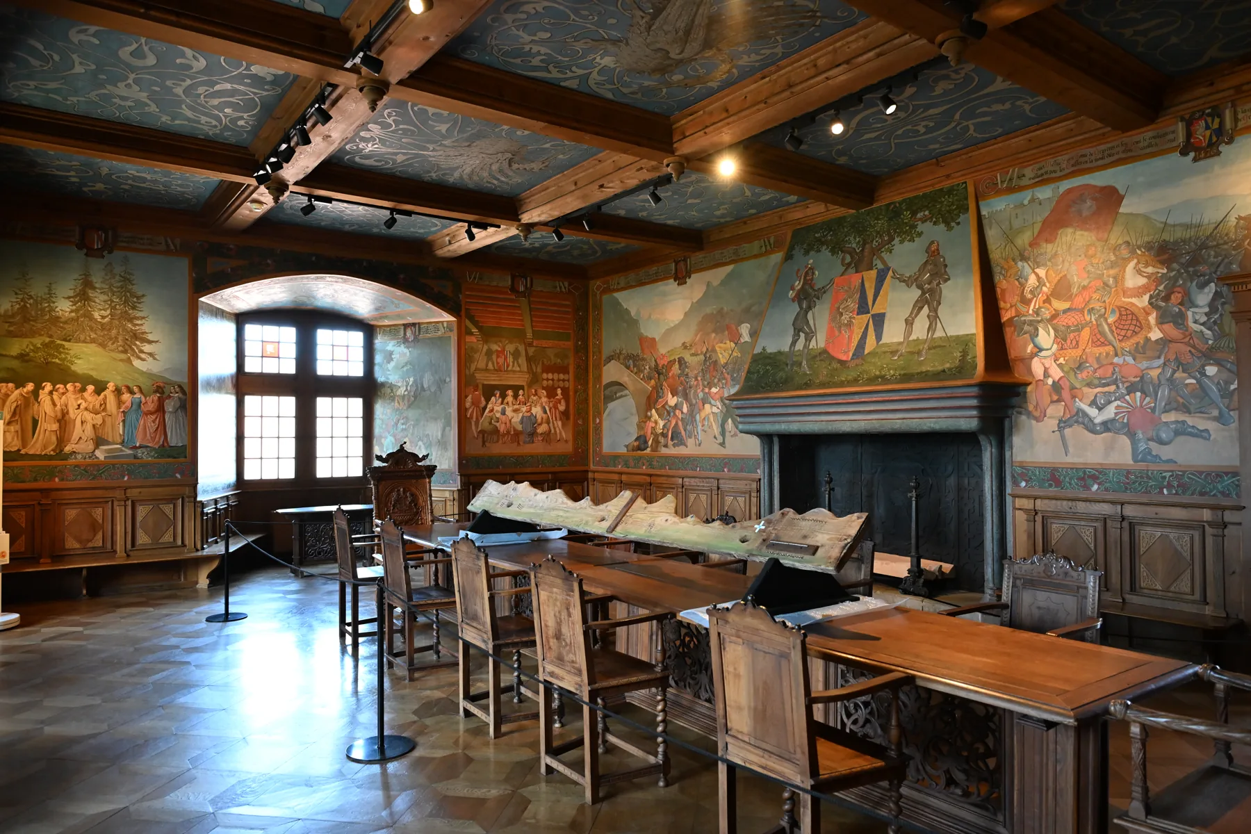 Sala do castelo com pinturas nas paredes, teto decorado e móveis de madeira