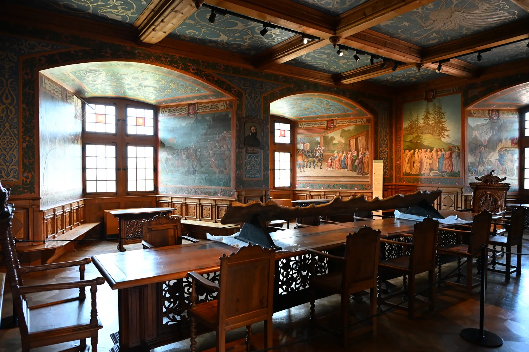 Vista das janelas, pinturas murais e mesas de uma sala do castelo