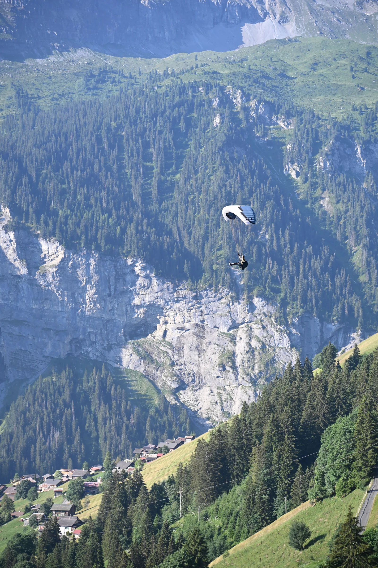 Parapente acima de encosta arborizada e casas do vale na região de Mürren