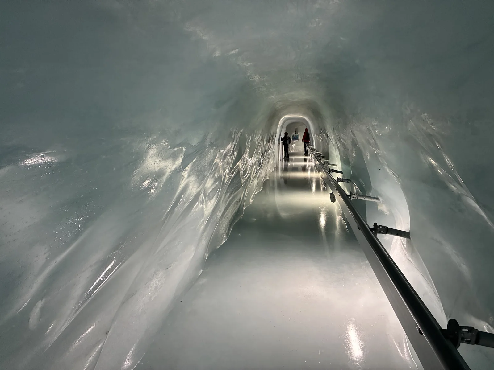 Túnel comprido de gelo com corrimão e visitantes ao fundo no Jungfraujoch